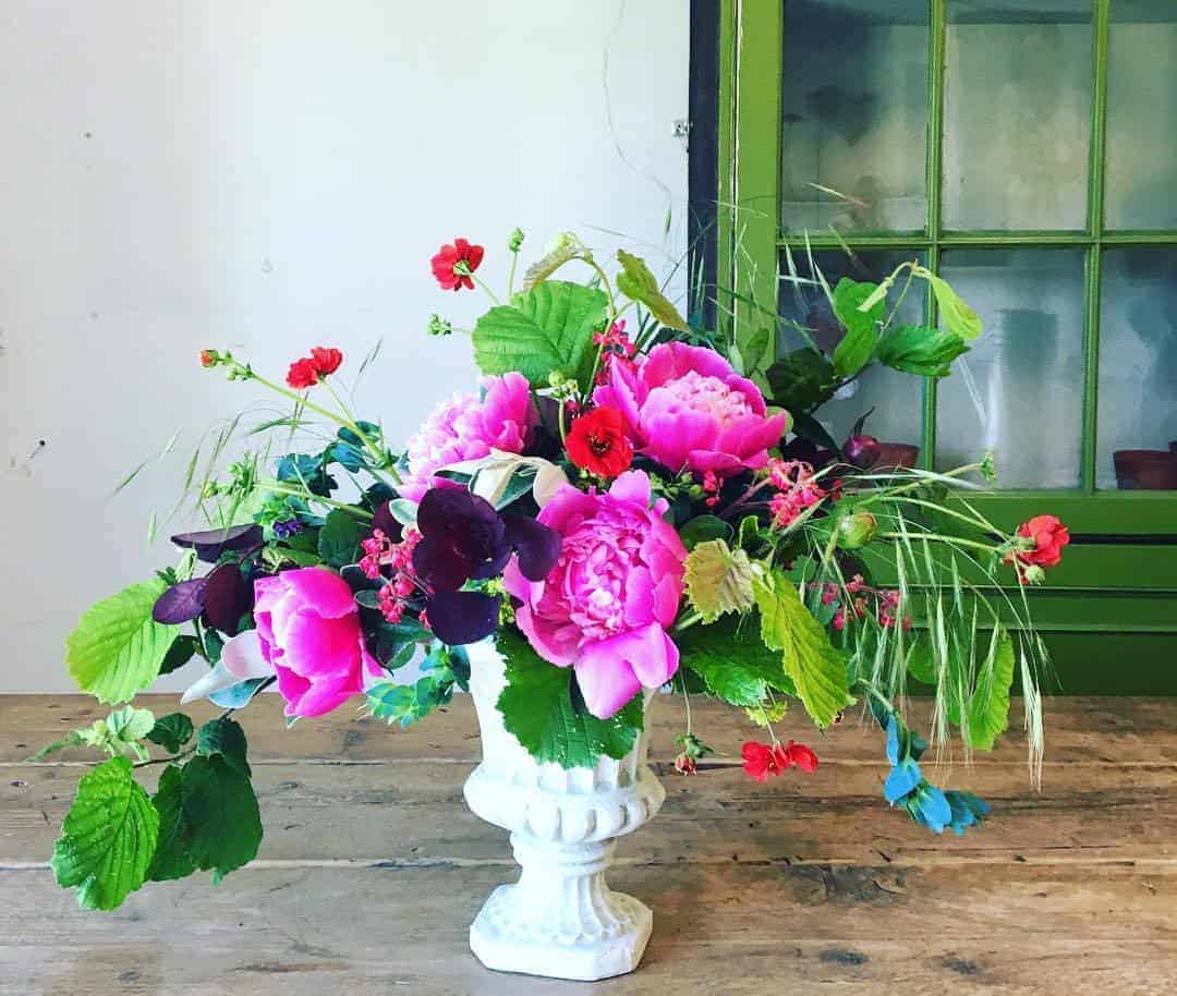 love this bright pink peonies with foraged foliage in white urn by Georgia of The Sussex Flower School. click through to find out more and to discover founder of the school, Georgia Miles' inspirations, simple pleasures and local loves